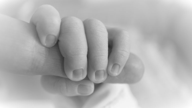 Black and white photo of baby grabbing parent's finger, contact